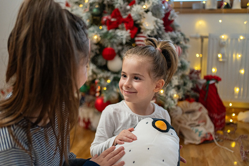 Adorable and excited toddler girl, showing to her older sister her new penguin toy she received as a Christmas gift