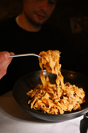 Close up of a man's hand eating Italian pasta pappardelle with a fork.