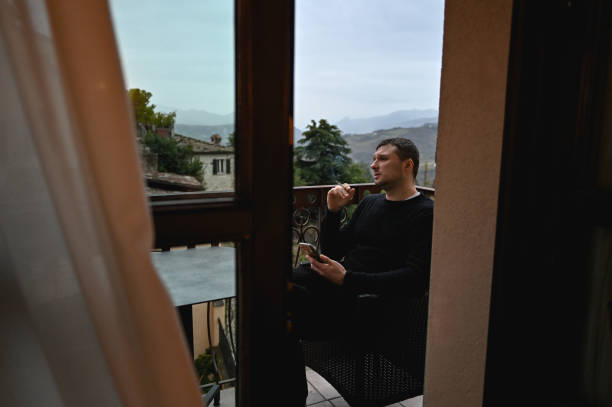 istock Serious man smoking at a balcony in hotel room. 1987864932