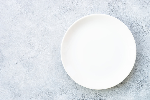 White plate at light stone table. Empty plate. Flat lay image.