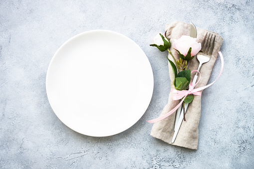 Spring Table setting with white plate, cutlery and flowers. Flat lay with at white with space for design.