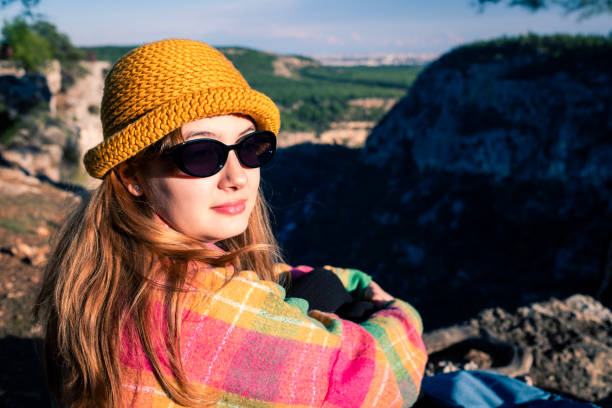 A young woman sitting under an old pine tree on the edge of a cliff.