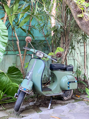 Yogyakarta, Indonesia - September 9, 2023: A green manual transmission motor scooter is parked in the yard with garden backgrounds. Concept for retro style transportation.