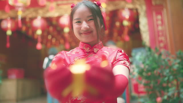 young asian girl in red Cheongsam gives you the gold ingot she is holding.smiling broadly and glancing at the camera.chinese new year concept.