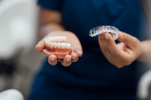 A medium close up of an orthodontist who is showing a patient some options for dental treat meant from their practice in the North East of England. Being shown are dental aligners and fixed braces.