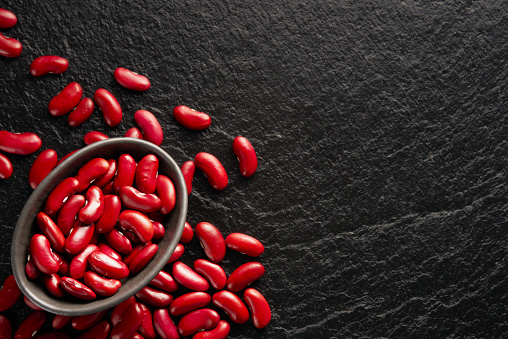 A bowl and a large group of red beans on a black stone background with copy space. Top view. Studio shot.