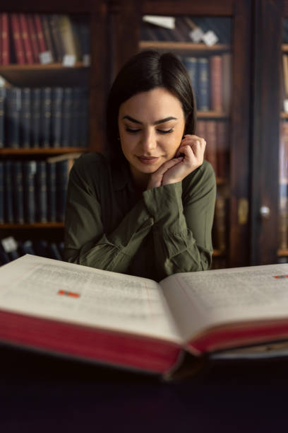 istock Beautiful young woman sitting and reading book in library 1987932968