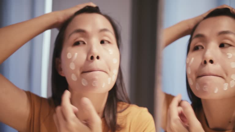 Radiant Beauty: Asian Woman Applying Gentle Skincare Lotion for Healthy, Glowing Skin.