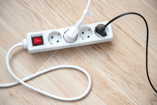 Pressing red button of a white power strip on wooden background - energy saving