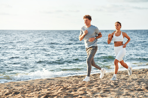 A couple in sportswear running along the shore by the sea. Morning exercises and jogging. Sports and recreation, active lifestyle.