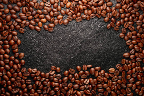 istock Large group of roasted coffee beans on a black stone background with space for text in the center. Top view. Studio shot. 1987941634