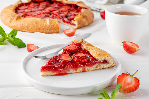 Galette, open pie or tart with strawberries with cup of tea on a white wooden table. Summer sweet pie