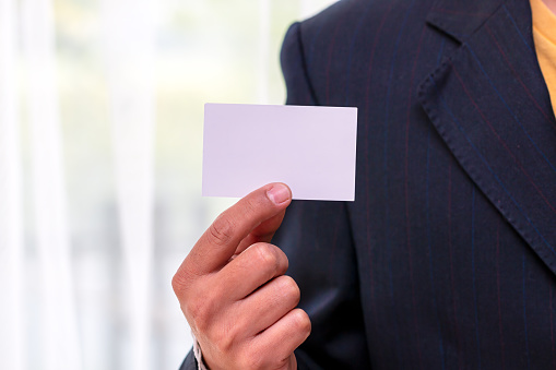 A detailed close-up of a businessman's hand offering a blank business card with copy space, illustrating the concept of corporate engagement and professionalism.