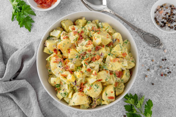 salad of potatoes, eggs, bacon and fresh herbs with mayonnaise and yogurt dressing in a bowl on a gray concrete background. - potatissallad bildbanksfoton och bilder