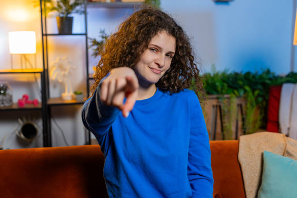 istock Happy woman sitting on sofa and pointing with both hands makes selecting and choosing gesture 1987961849