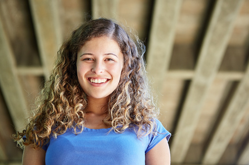 Happy young woman smiles down at you, with a concrete bridge above her.