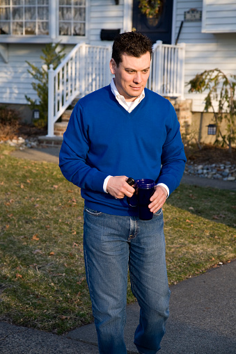Handsome thirty something man holding coffee cup and car keys, leaving for work on a beautiful sunny morning.