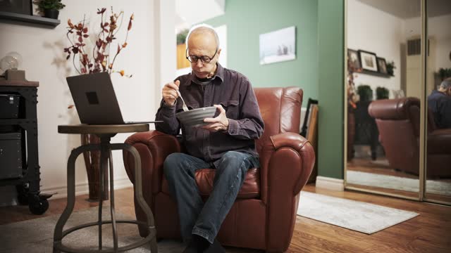 Senior man having a salad meal while using laptop in his living room