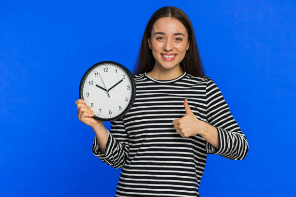 kobieta rasy kaukaskiej pokazująca godzinę godziny na zegarze ściennym, ok, kciuk w górę, zatwierdzić, pospiesz się, termin - checking the time time clock women zdjęcia i obrazy z banku zdjęć