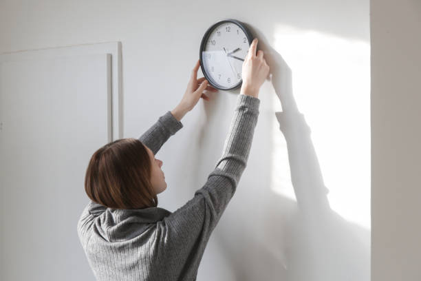 istock Young woman hanging clock on the wall, back view 1987995782