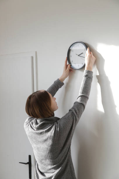istock Young woman hanging clock on the wall, back view 1987996382