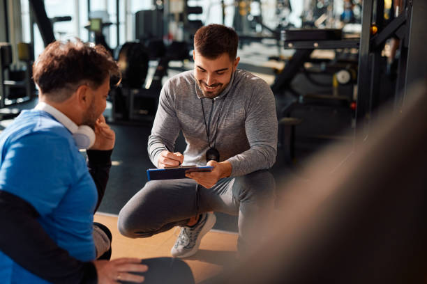 istock Young happy coach making exercise plan during mature man's sports training in a gym. 1988003585