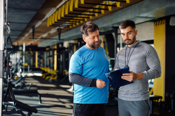 istock Mature man and his personal trainer making exercise plan for gym workout. 1988013971