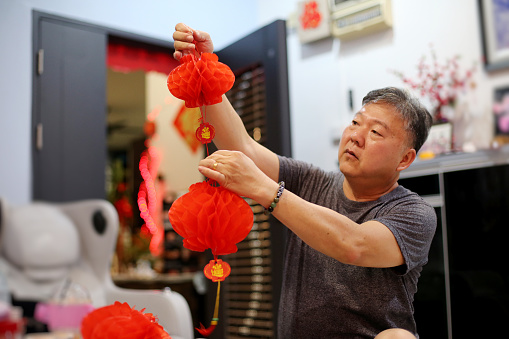 An Asian senior man is preparing Chinese New Year decoration at home