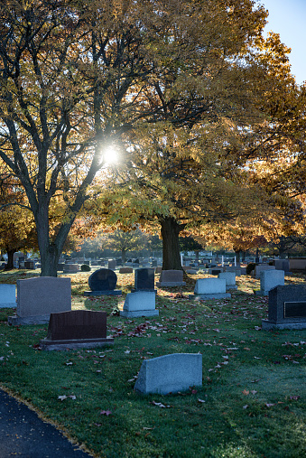 Early morning starburst sunlight filtering through tree branches and leaves in early autumn above a quiet rural cemetery in western New York State near Rochester.