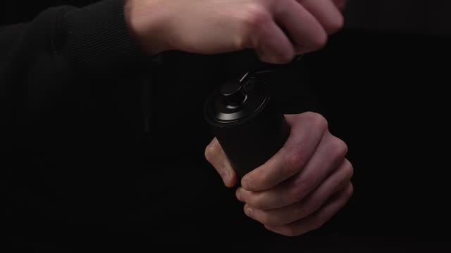 Close-up male hands grinding coffee on a modern manual steel coffee grinder on black background