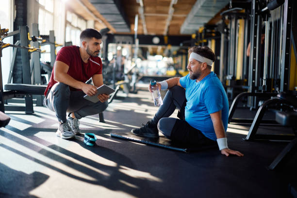 istock Mature athlete talking to his personal trainer while having water break in a gym. 1988018891