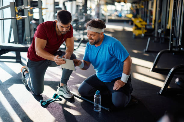 istock Happy mature athlete and his personal trainer using touchpad in a gym. 1988019392