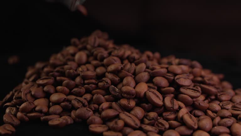 Coffee beans pour out of a glass jar falling on coffee surface in slow motion