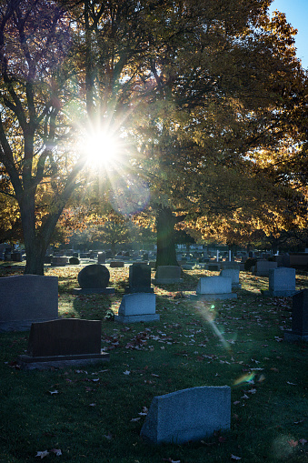 Early morning starburst sunlight filtering through dark tree branches and leaves in early autumn above a quiet rural cemetery in western New York State near Rochester in late October. Some grain in this image.