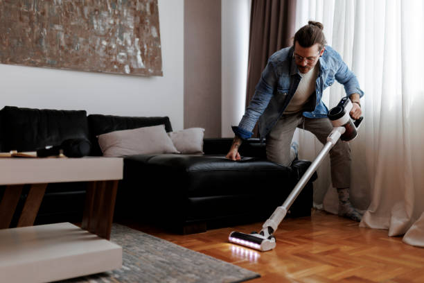 istock Man cleaning house with wireless vacuum cleaner 1988029819