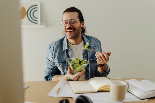 Man using computer, learning, working and eating snack salad at home office