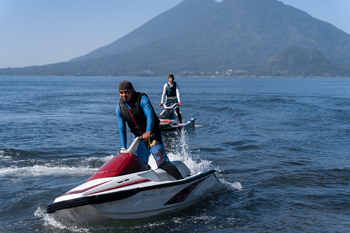 Two young Hispanic men navigate jet-skis on the waters of Atitlan Lake, Guatemala, engaging in recreational water activity against the scenic backdrop of the lake's natural beauty
