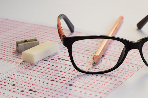Black color glasses,wooden pencil and rubber on filled exam sheet,conceptual image of education qualifying test exam.
