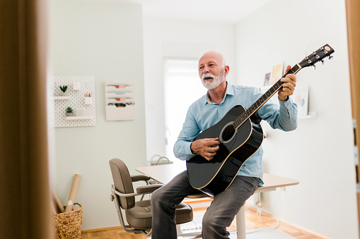 Senior male playing guitar at home office