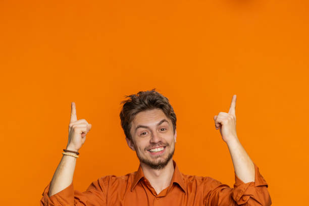 istock Young man showing promotion, pointing overhead up on blank space place for your advertisement logo 1988077842