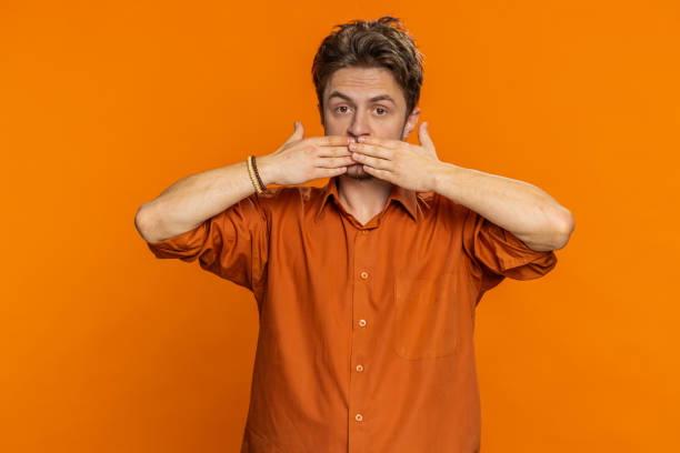 istock Frightened young man closing mouth with hands refusing to tell terrible secret unbelievable truth 1988078152