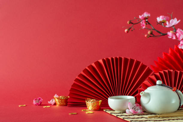 Oriental New Year side view scene with feng shui decor, gold coins, tea set, cherry blossoms, and fans on a vibrant red backdropâperfect for festive greetings or promotions