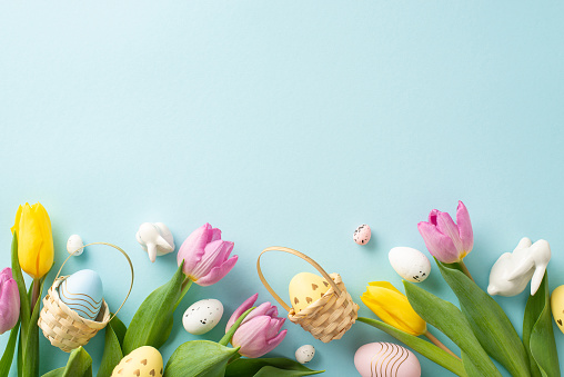 Delightful Easter Atmosphere: Top view of eggs in a charming baskets, cute bunnies, and fresh tulips on a serene blue background. Great for text or promotional content