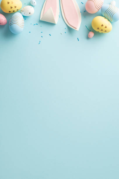 Springtime Happiness Display: Vertical top view of eggs, cute bunny ears, festive sprinkles on a gentle sky blue backdrop. Perfect for messages or advertisements with available text space