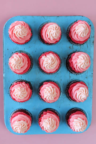 image de turquoise, plaque de cuisson à muffins avec des rangées de cupcakes en velours rouge faits maison dans des caisses à gâteaux en papier, décorées de tourbillons pipés au beurre rose à effet ombré, fond rose, vue surélevée, concept de la  - valentines day nobody plaque studio shot photos et images de collection