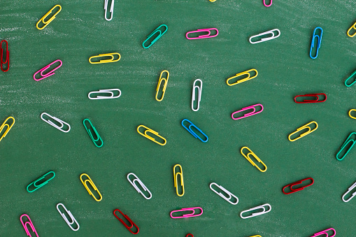 Colorful metal paper clips on green chalkboard with chalk trail,top view.Conceptual image of education backgrounds.