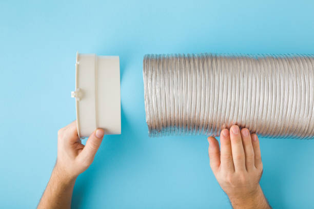 istock Man hands holding plastic adapter and corrugated aluminium pipe on blue wall background. Point of view shot. Assembling new ventilation parts for kitchen cooker hood or air conditioning. Closeup. 1988166167