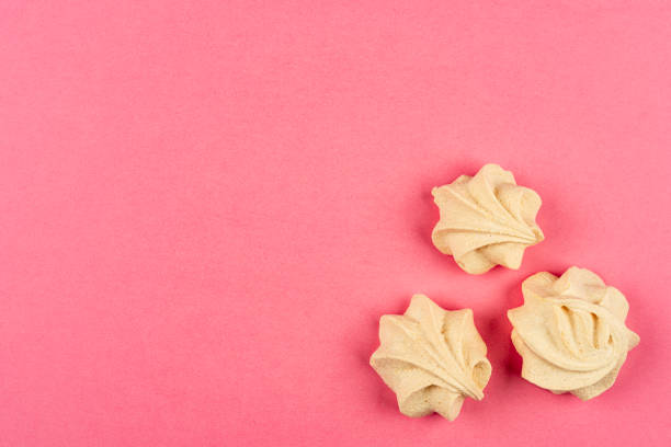 White marshmallow on pink background in white wrapper, white marshmallow in paper tartlet, delicate dessert on pink background