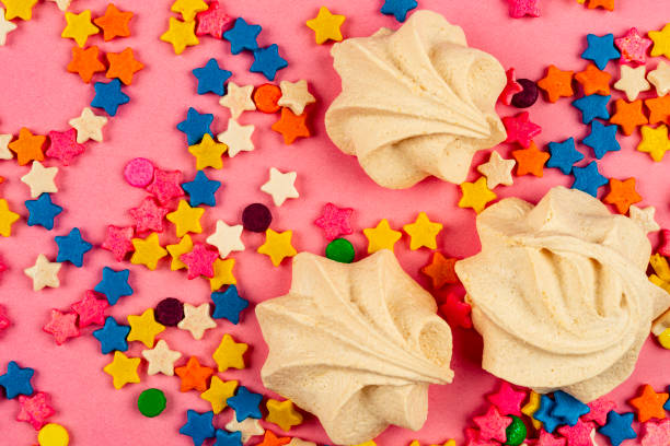 High angle view of homemade meringue cookies on a cooling rack with natural baking ingredients including sugar, eggs, dark chocolate, cinnamon sticks, and star anise on a rustic blue wooden surface. The scene highlights a sustainable, mindful approach to baking with real ingredients and minimal waste. Warm textures and earthy tones convey a cozy, handcrafted mood. Copy space available on the lower and right side of the image.