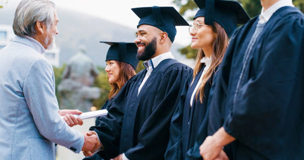 istock Professor, graduation and students for giving diploma, handshake and congratulations for achievement. Senior lecturer, men and woman with shaking hands, certificate or happy for success at university 1988194349
